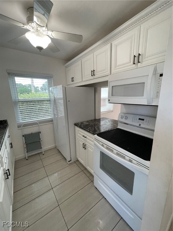 Kitchen featuring white appliances, white cabinets, dark stone counters, a ceiling fan, and light tile patterned floors