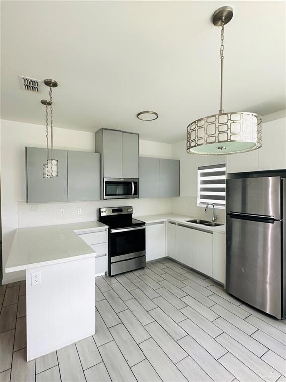 Kitchen featuring a peninsula, a sink, visible vents, decorative light fixtures, and appliances with stainless steel finishes
