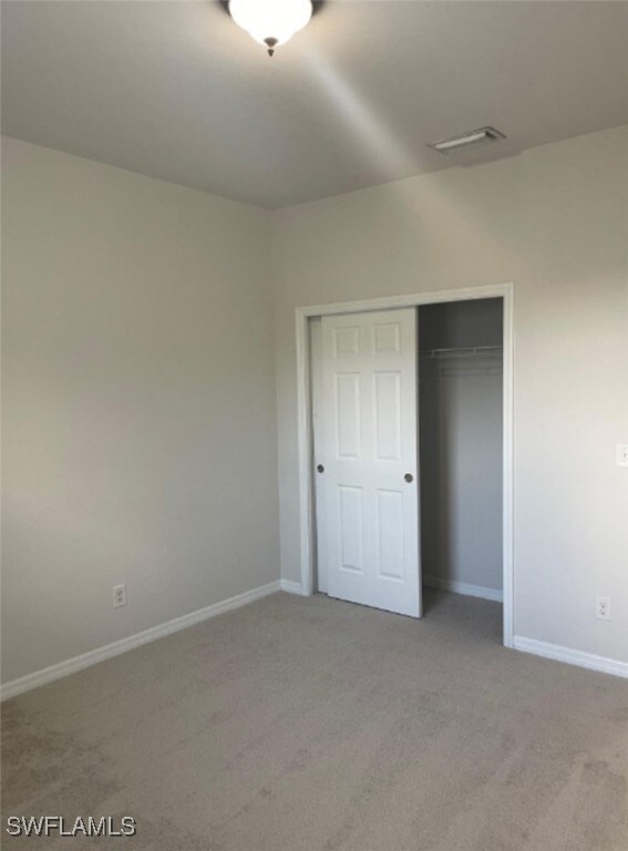 Unfurnished bedroom with light carpet and a closet