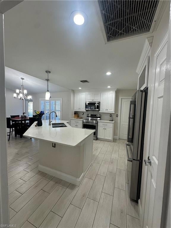 Kitchen featuring sink, white cabinetry, range, fridge, and an island with sink