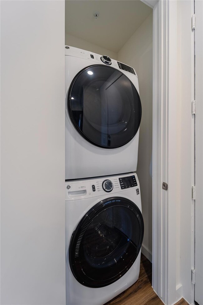 Laundry room with wood finished floors, stacked w