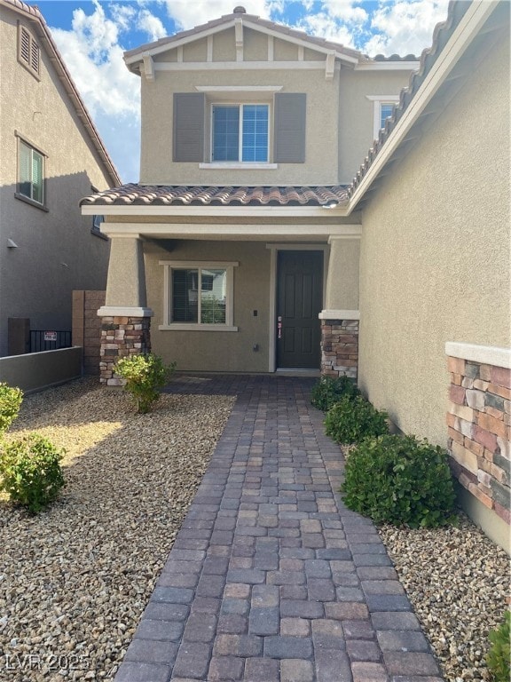 Entrance to property featuring stone siding, stucco siding, a tile roof, and covered porch