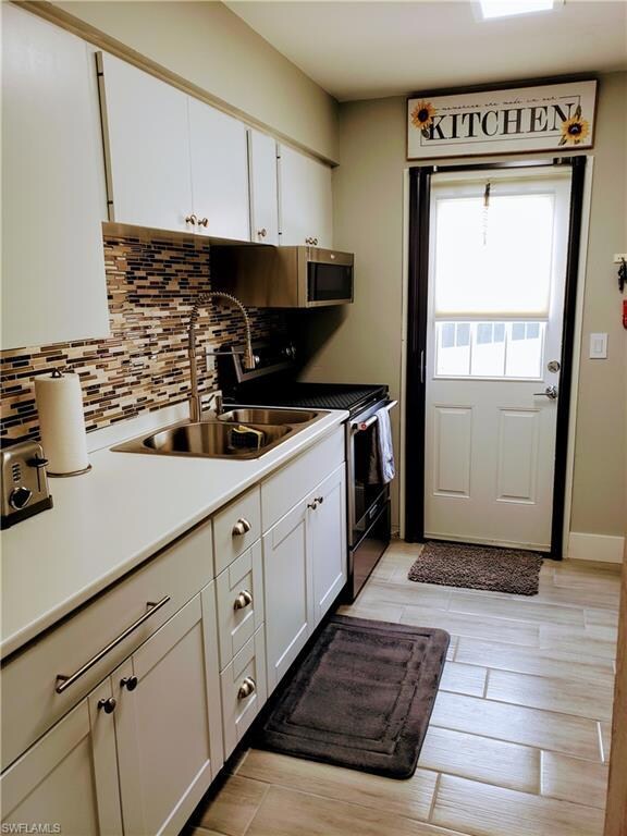 Kitchen featuring stainless steel appliances, a sink, backsplash, white cabinetry, and light wood-type flooring