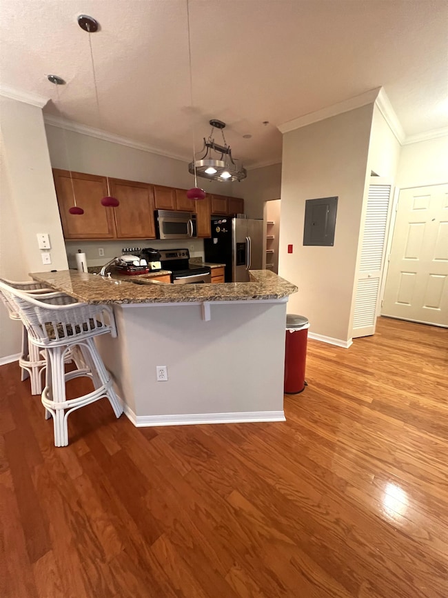 Kitchen with a kitchen breakfast bar, ornamental molding, a peninsula, brown cabinets, and pendant lighting