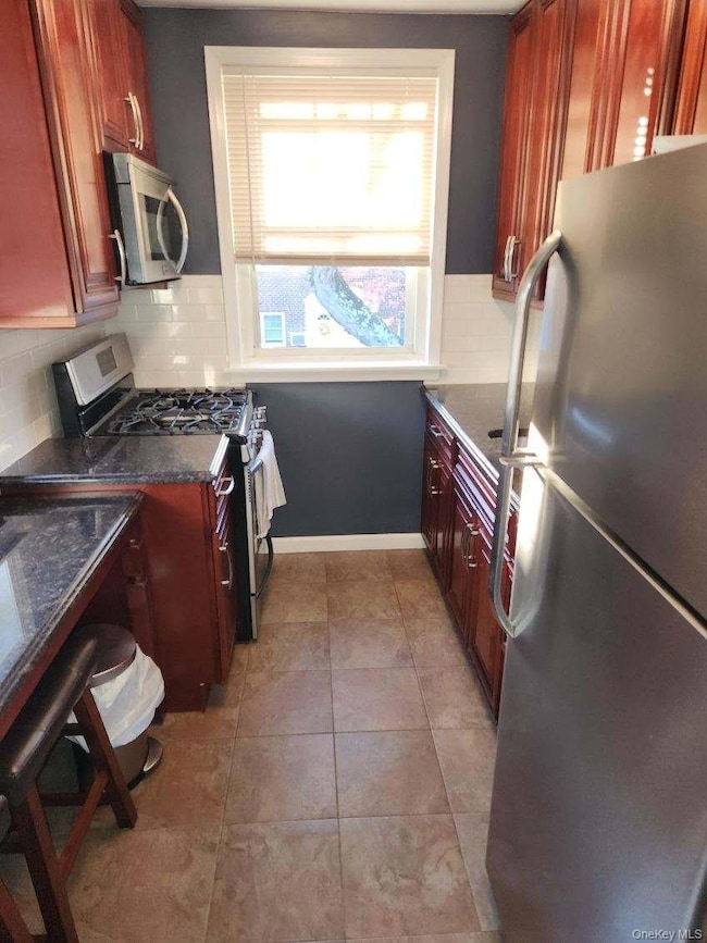 Kitchen with appliances with stainless steel finishes, dark brown cabinets, dark stone countertops, and decorative backsplash