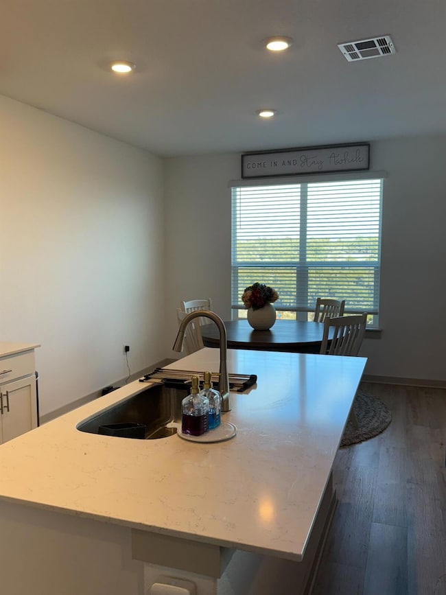 Kitchen featuring a kitchen island with sink, recessed lighting, light stone counters, dark wood-type flooring, and white cabinets