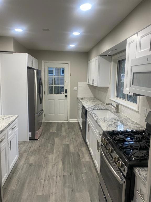 Kitchen featuring stainless steel appliances, a sink, white cabinetry, light stone countertops, and wood finished floors