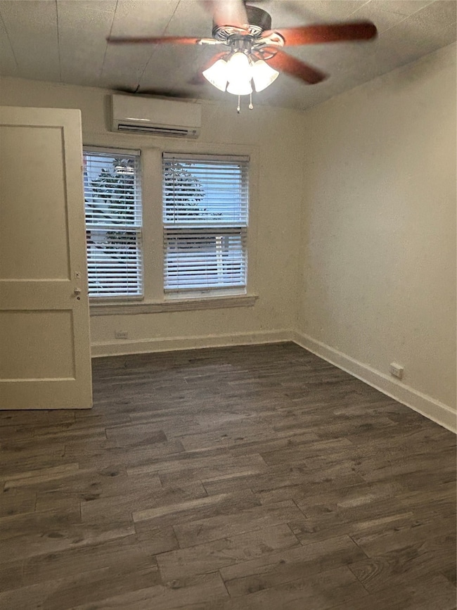 Spare room featuring dark wood-type flooring, healthy amount of natural light, a wall mounted air conditioner, and ceiling fan