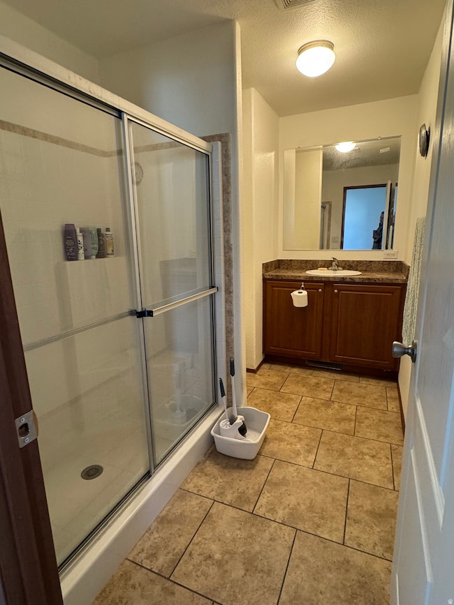 Full bath with a textured ceiling, vanity, a shower stall, and light tile patterned floors