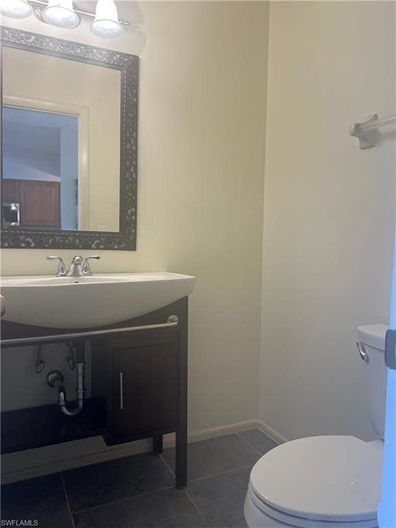 Half bath featuring toilet, tile patterned floors, vanity, and baseboards
