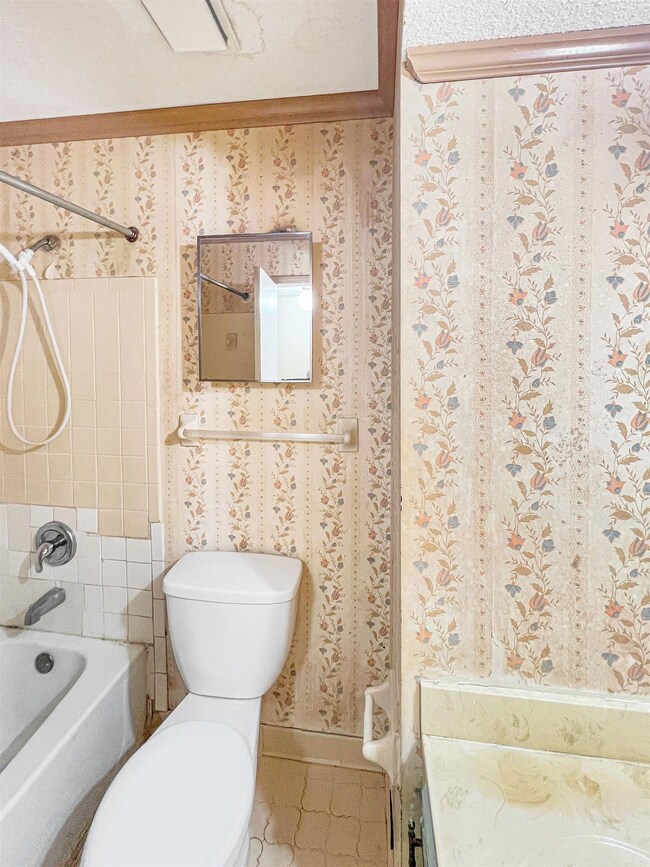 Bathroom with wallpapered walls, toilet, and showe