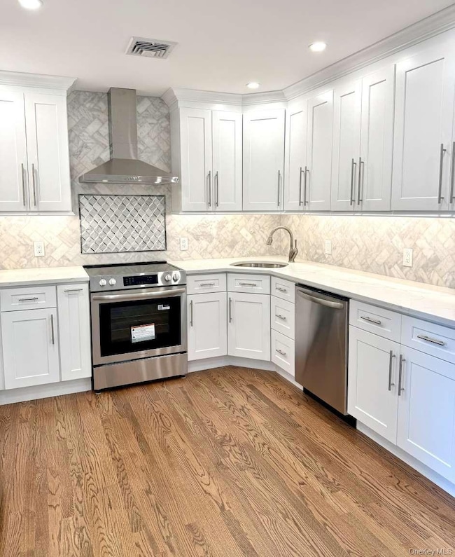 Kitchen with appliances with stainless steel finishes, wall chimney range hood, tasteful backsplash, white cabinets, and recessed lighting