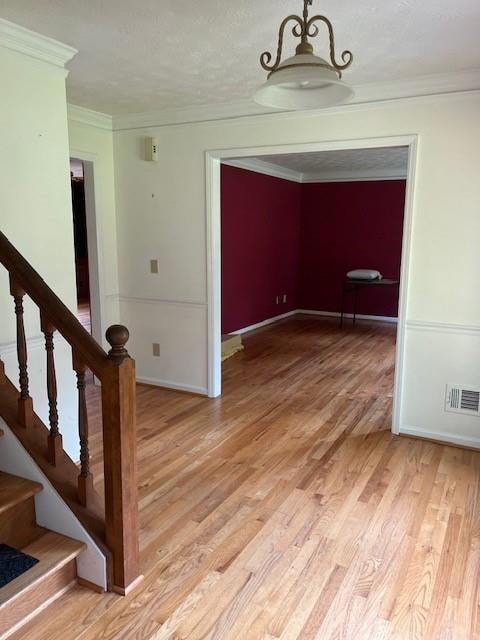 Spare room with crown molding, light wood-style flooring, stairway, and baseboards