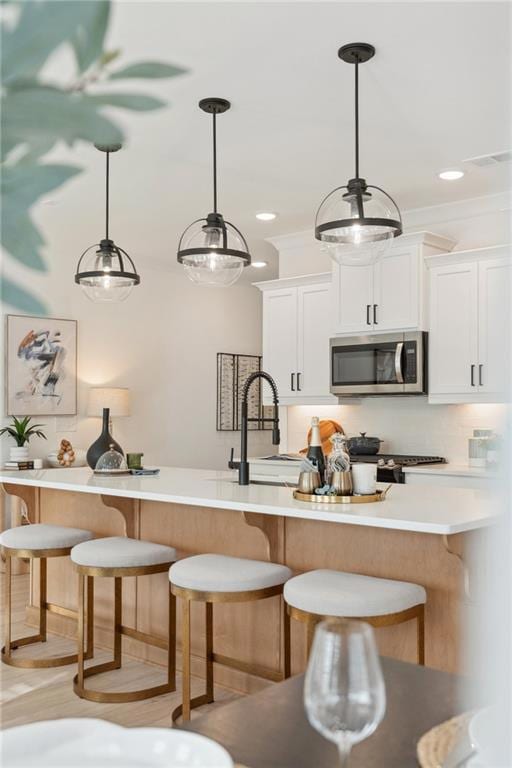 Kitchen with stainless steel microwave, a breakfast bar area, light countertops, decorative backsplash, and decorative light fixtures