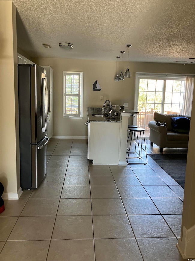 Kitchen featuring tile patterned flooring, a textured ceiling, freestanding refrigerator, white cabinets, and a kitchen bar