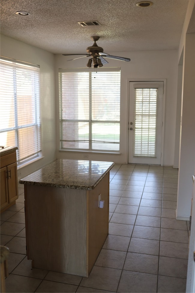 Kitchen with a textured ceiling, light tile patterned flooring, ceiling fan, a kitchen island, and light stone countertops