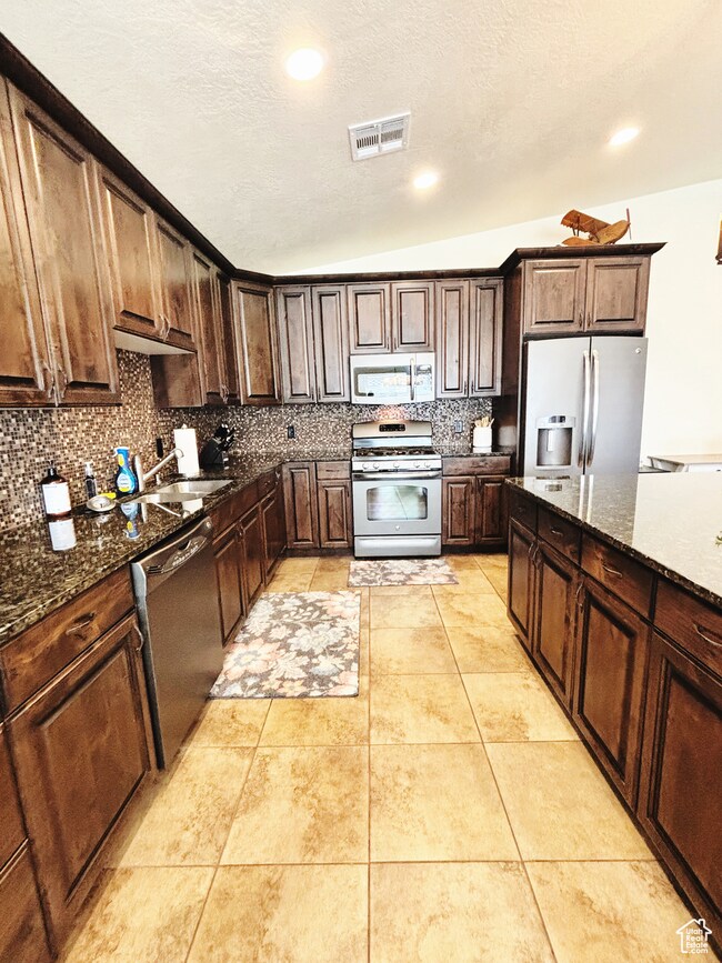Kitchen featuring stainless steel appliances, tasteful backsplash, dark stone counters, recessed lighting, and dark brown cabinets