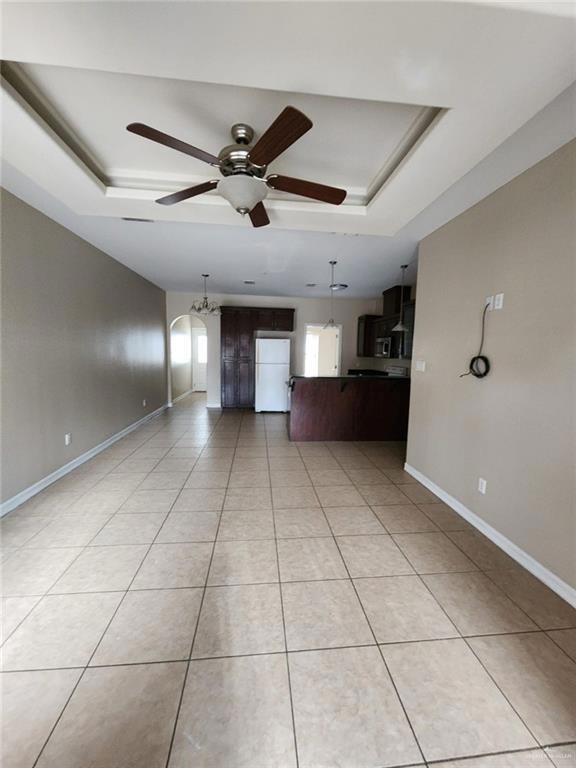 Empty room featuring light tile flooring, ceiling fan, and a tray ceiling