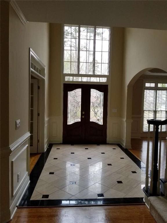 Entrance foyer featuring arched walkways, inlaid floor details, tile patterned floors, french doors, and a decorative wall