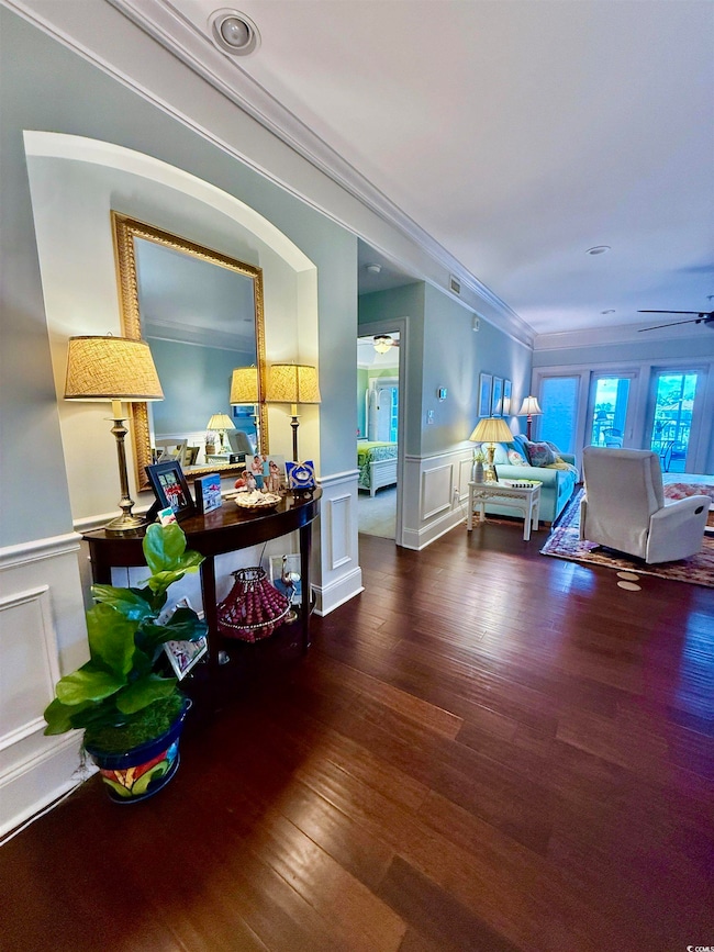 Corridor featuring a wainscoted wall, a decorative wall, wood finished floors, and ornamental molding