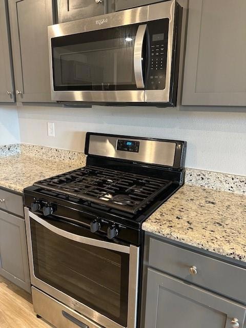 Detailed view of stainless steel gas range, gray cabinetry, light stone countertops, and light wood-style floors