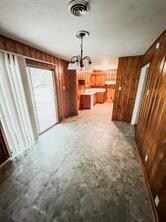 Unfurnished living room featuring wooden walls and a chandelier