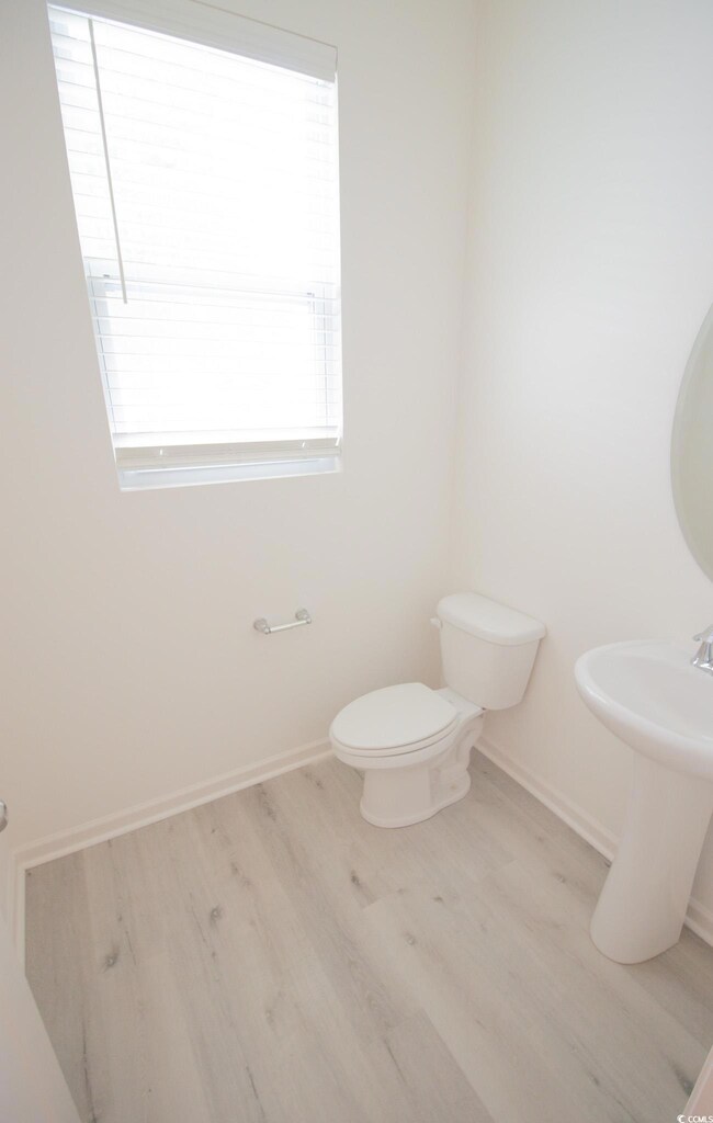 Half bathroom with wood finished floors, baseboards, and toilet