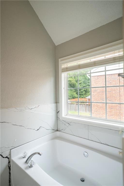 Full bath featuring a bath, a textured wall, and lofted ceiling