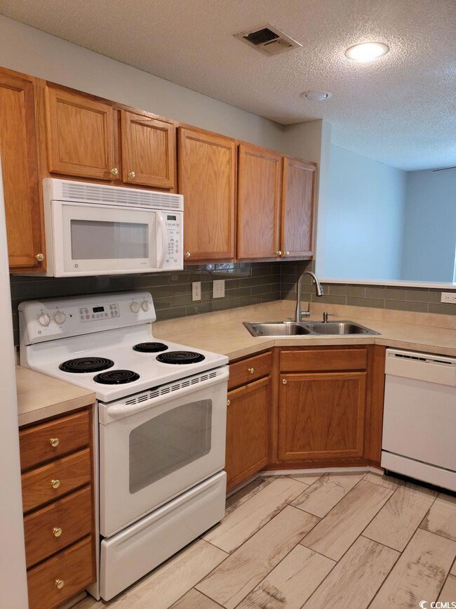 Kitchen with backsplash, sink, white appliances, and a textured ceiling