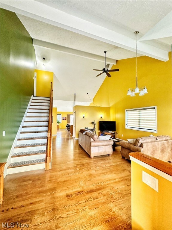 Living room featuring ceiling fan with notable chandelier, light hardwood / wood-style flooring, beam ceiling, and a textured ceiling