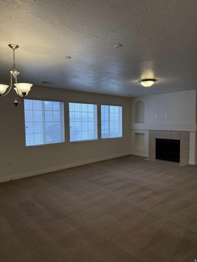 Unfurnished living room with carpet, a textured ceiling, a tile fireplace, and a chandelier