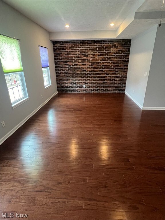 Spare room with brick wall and dark hardwood / wood-style flooring
