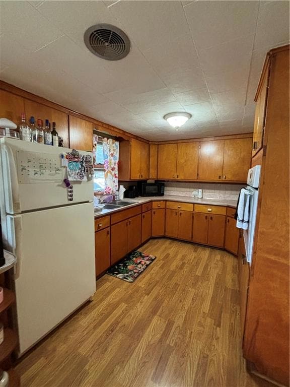 Kitchen with wall oven, sink, light hardwood / wood-style floors, and refrigerator