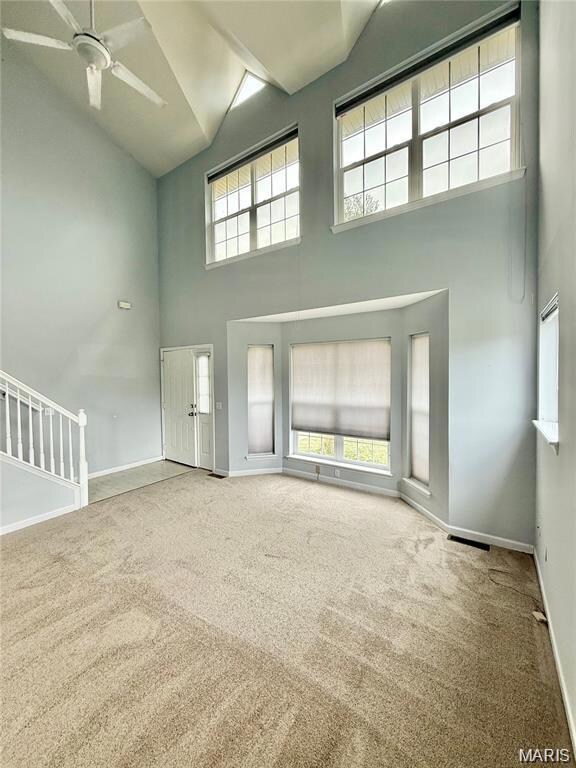 Unfurnished living room featuring high vaulted ceiling, healthy amount of natural light, carpet flooring, and stairs