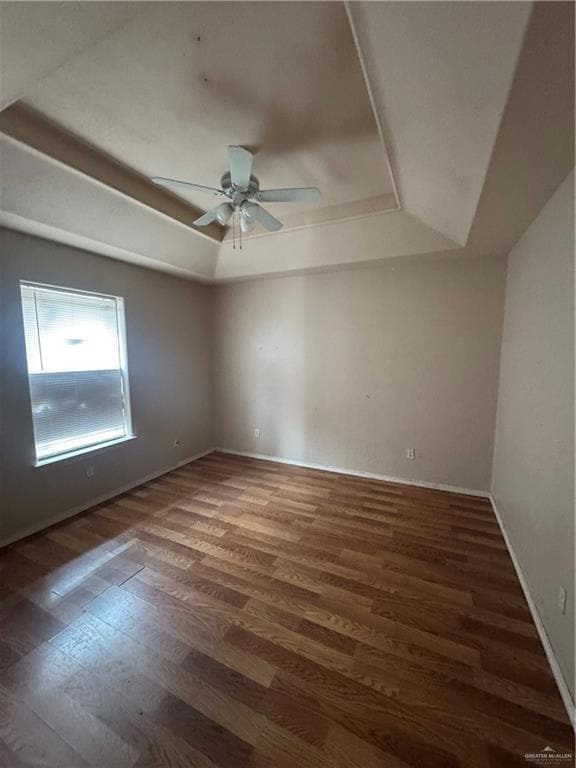 Spare room featuring a raised ceiling, wood finished floors, a ceiling fan, and baseboards