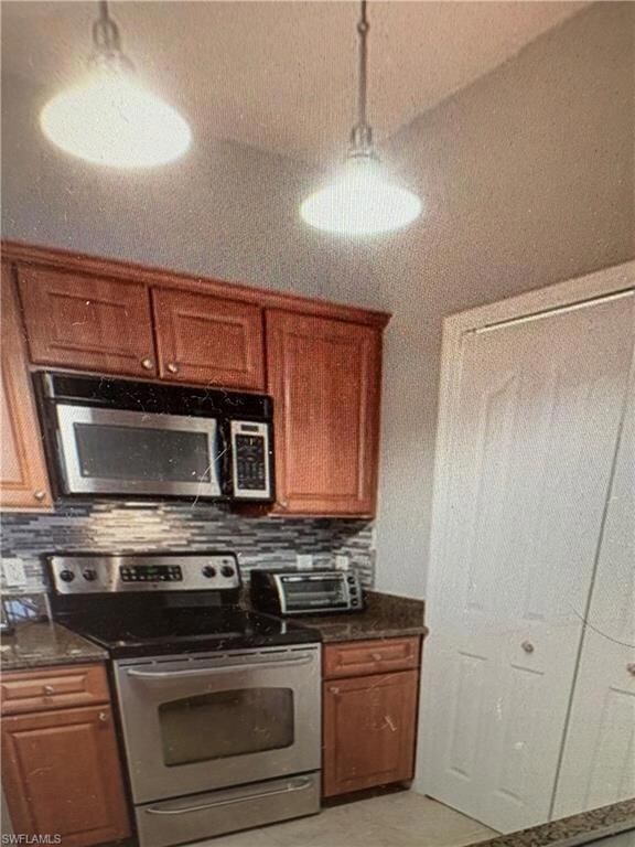 Kitchen with appliances with stainless steel finishes, backsplash, brown cabinetry, and dark stone counters