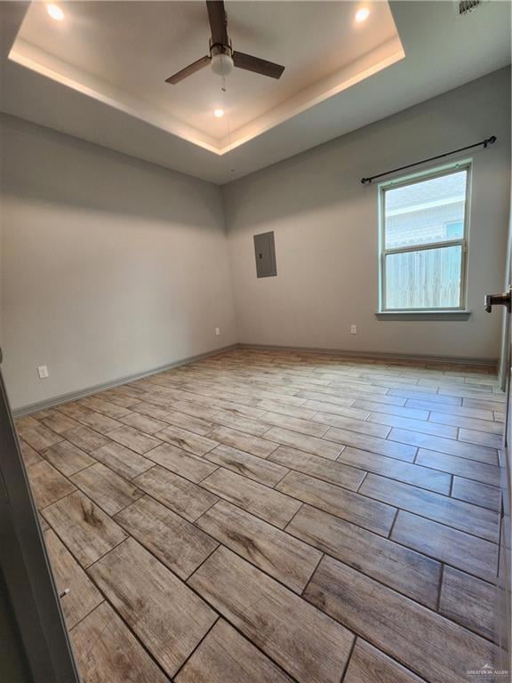 Empty room with a tray ceiling, recessed lighting, ceiling fan, wood finished floors, and electric panel