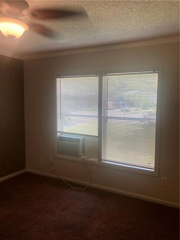 Unfurnished room with dark carpet, healthy amount of natural light, a textured ceiling, crown molding, and cooling unit