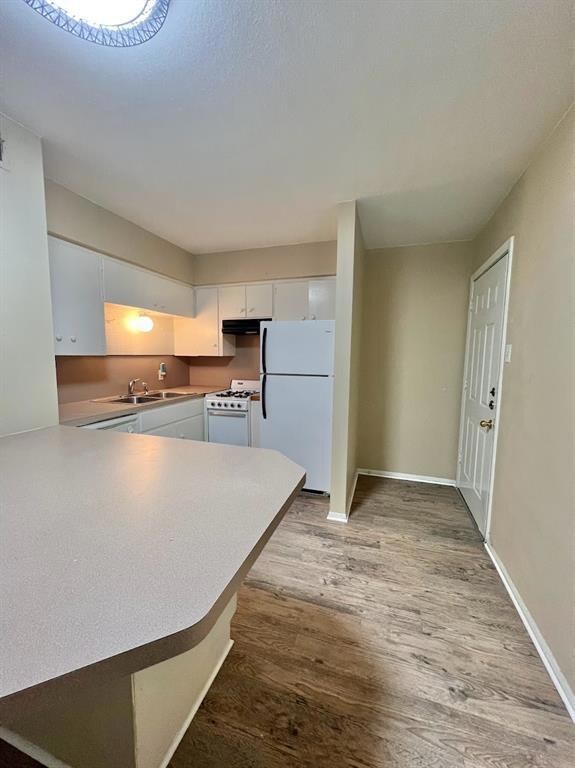 Kitchen with light wood-style floors, white appliances, white cabinetry, light countertops, and a peninsula