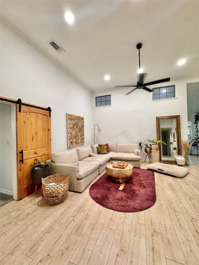 Living room with a barn door, a ceiling fan, wood finished floors, ornamental molding, and recessed lighting