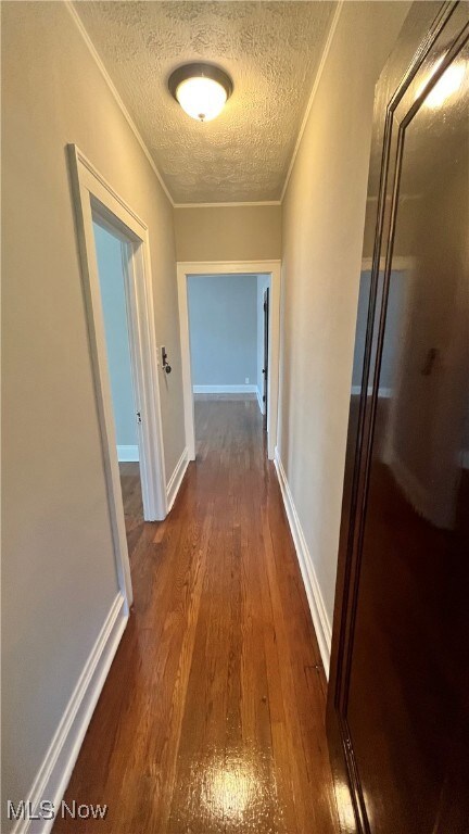 Hall with dark wood-style floors, a textured ceiling, and ornamental molding