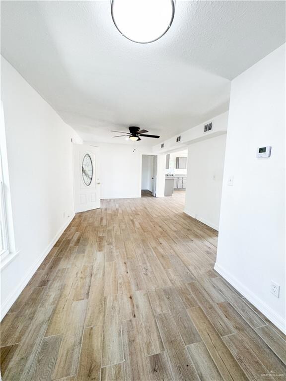Unfurnished living room with a textured ceiling, light hardwood / wood-style floors, and ceiling fan