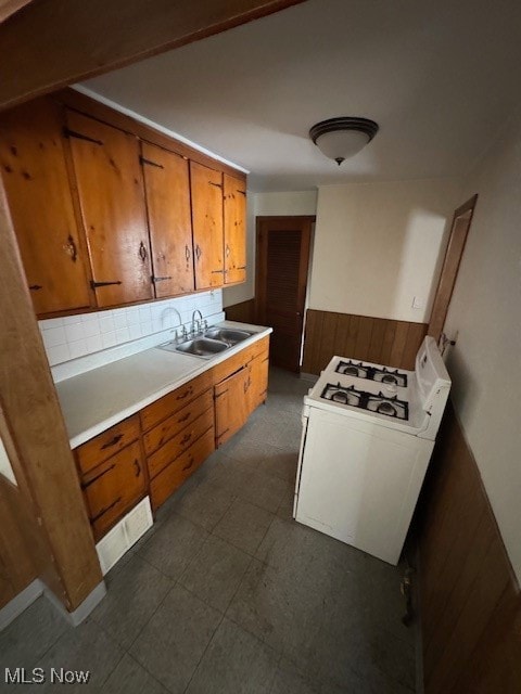 Kitchen featuring light countertops, range, wainscoting, wood walls, and brown cabinetry