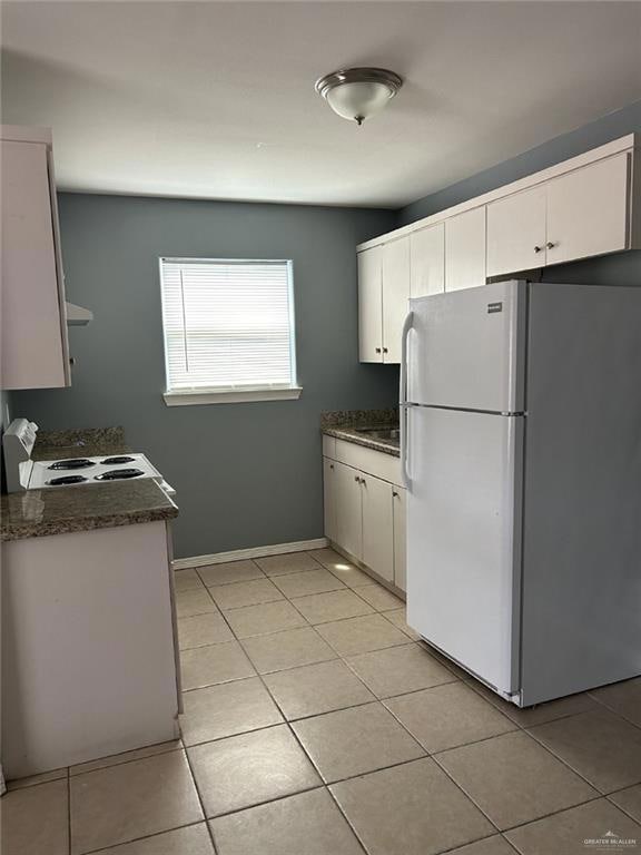 Kitchen with white appliances, dark countertops, light tile patterned floors, white cabinets, and baseboards