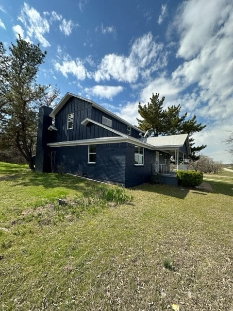 View of side of home featuring board and batten siding, a lawn, and brick siding