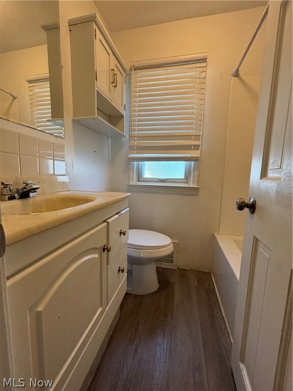Full bathroom with bathing tub / shower combination, wood-type flooring, vanity with extensive cabinet space, tasteful backsplash, and toilet