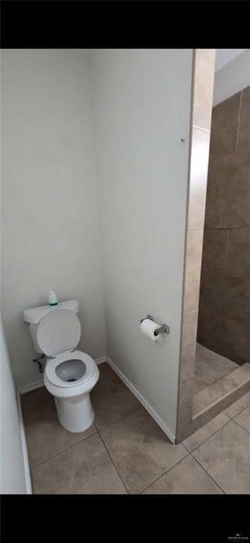 Full bath with tile patterned floors, toilet, tiled shower, and baseboards