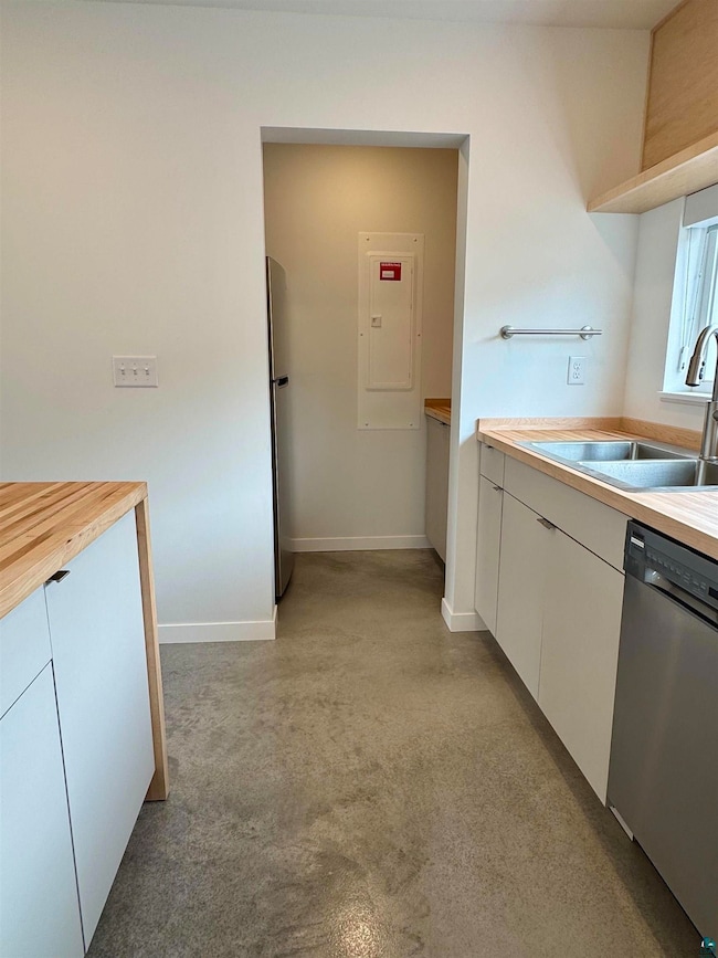 Kitchen featuring dishwasher, white cabinets, electric panel, and wood counters