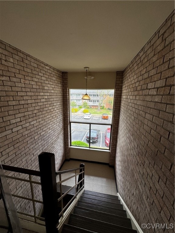 Stairway with tile patterned floors and brick wall