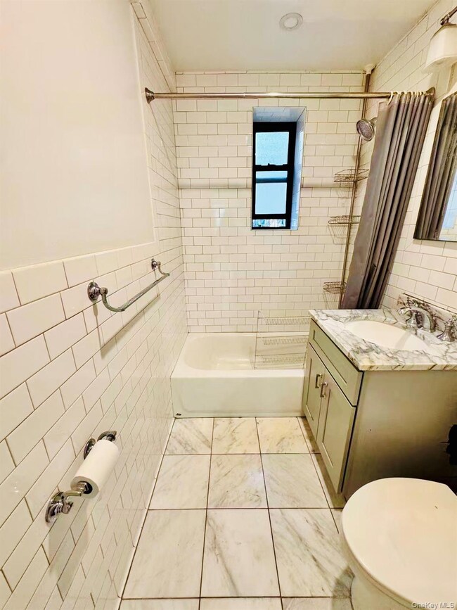 Bathroom featuring tile walls, shower / bath combo, vanity, and light tile patterned flooring